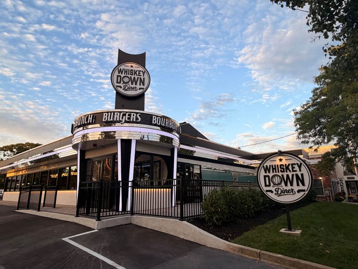 The Whiskey Down Diner sign lit above the Babylon Village entrance at dusk
