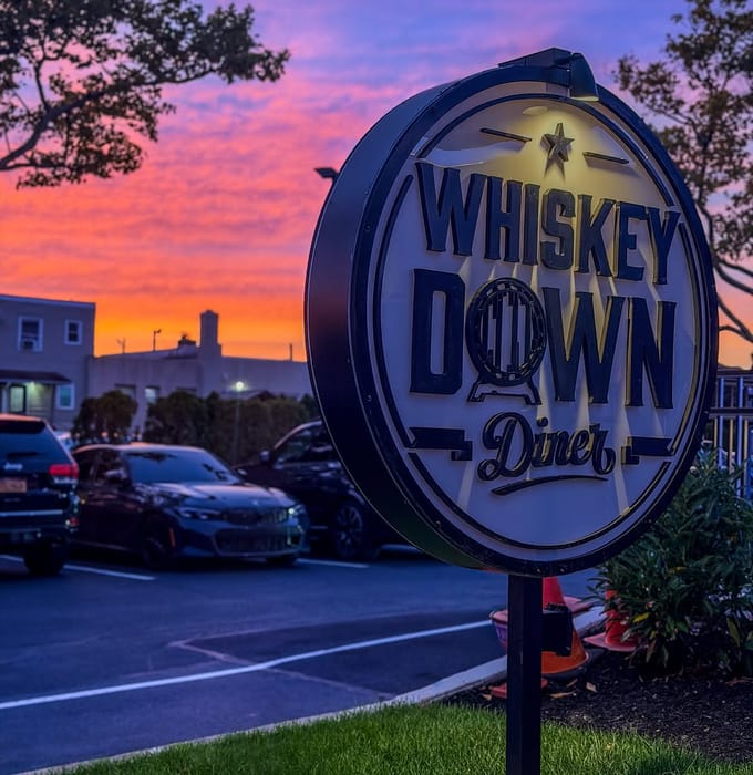 The Whiskey Down Diner sign in Babylon Village against a sunset sky